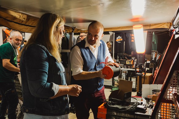 Mężczyzna przedstawiający działanie narzędzia podczas targów, kobiecie ubranej w jeansową katane. Na zaaranżowanym stoisku targowym.